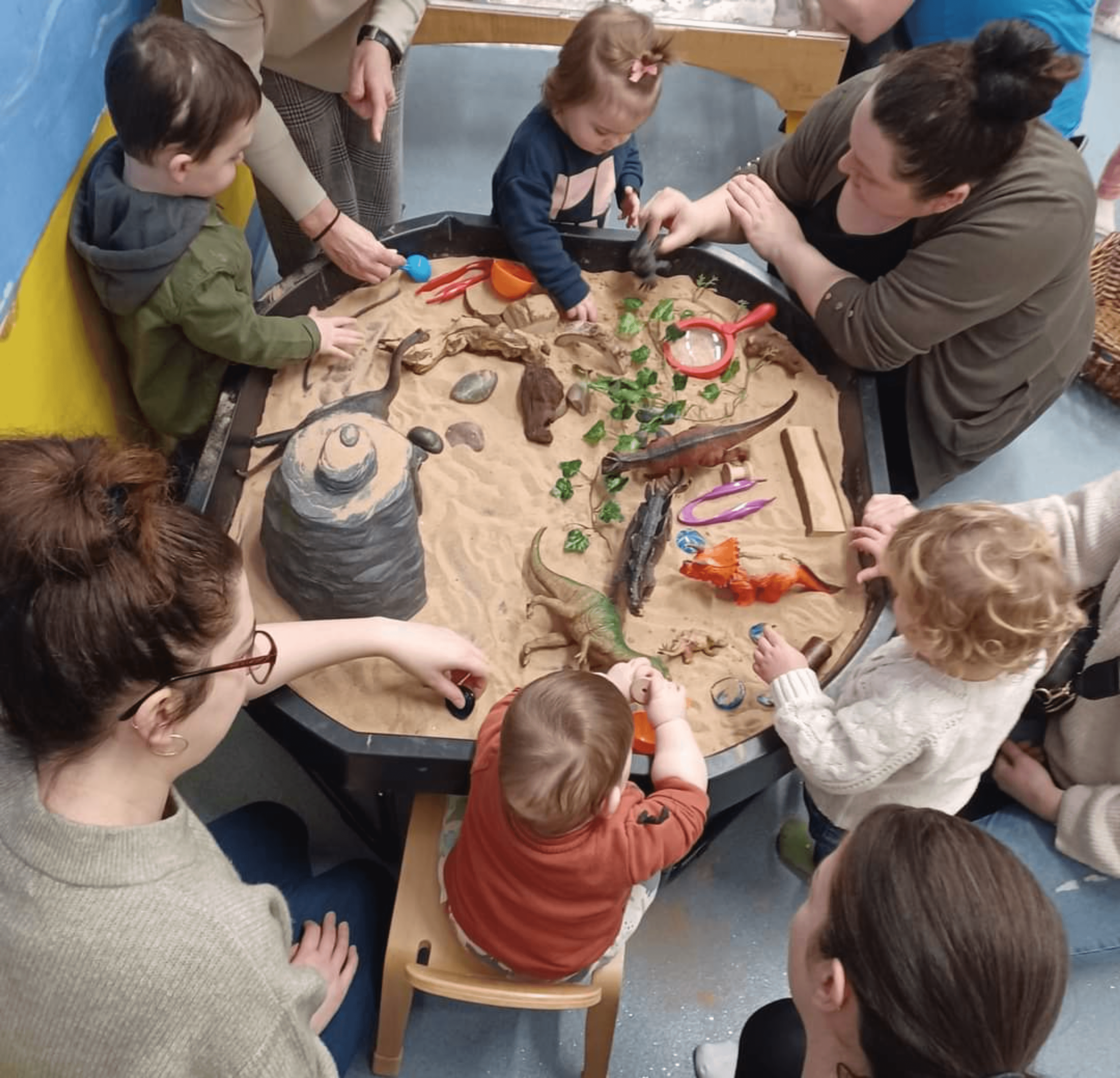 Parents and children around a sand tray with dinosaurs